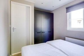 A bedroom with a bed, a wardrobe, and a window. - Cube XL 71 | 4 persoons chalet in Zennewijnen (Zennewijnen)