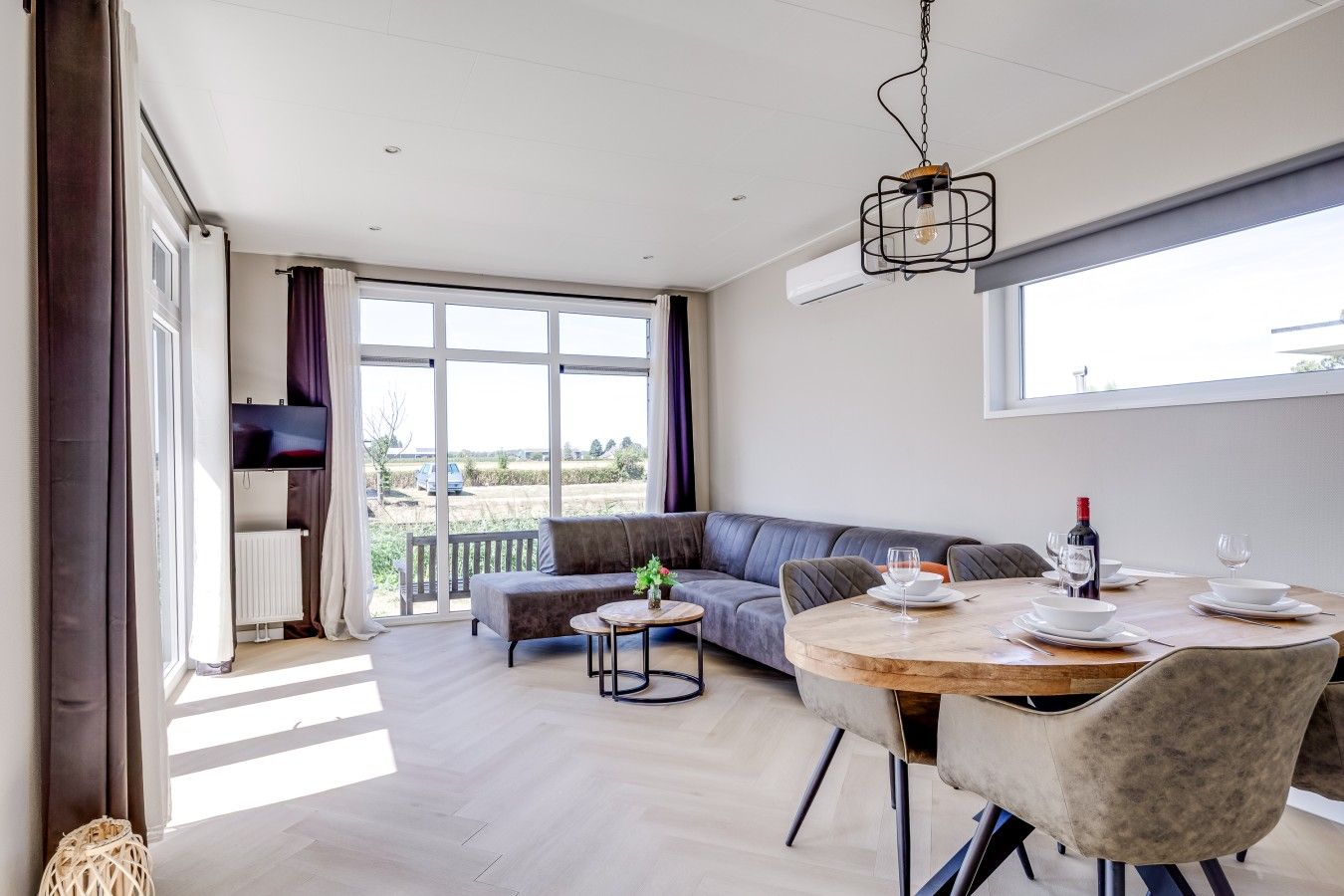 Un salon moderne avec un canapé, une table à manger pour deux personnes et un téléviseur fixé au mur.