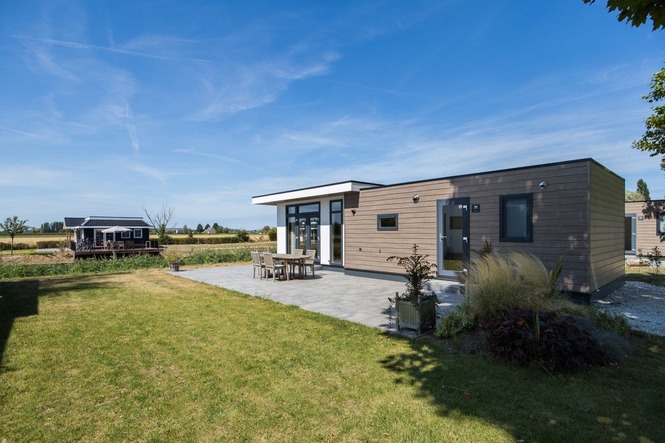 A modern two-story house with a patio, a deck, and a view of the surrounding countryside.
