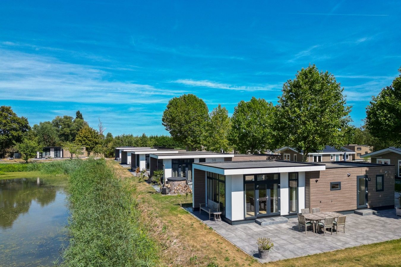Un vecindario residencial moderno con varias casas, un estanque y un cielo azul despejado.