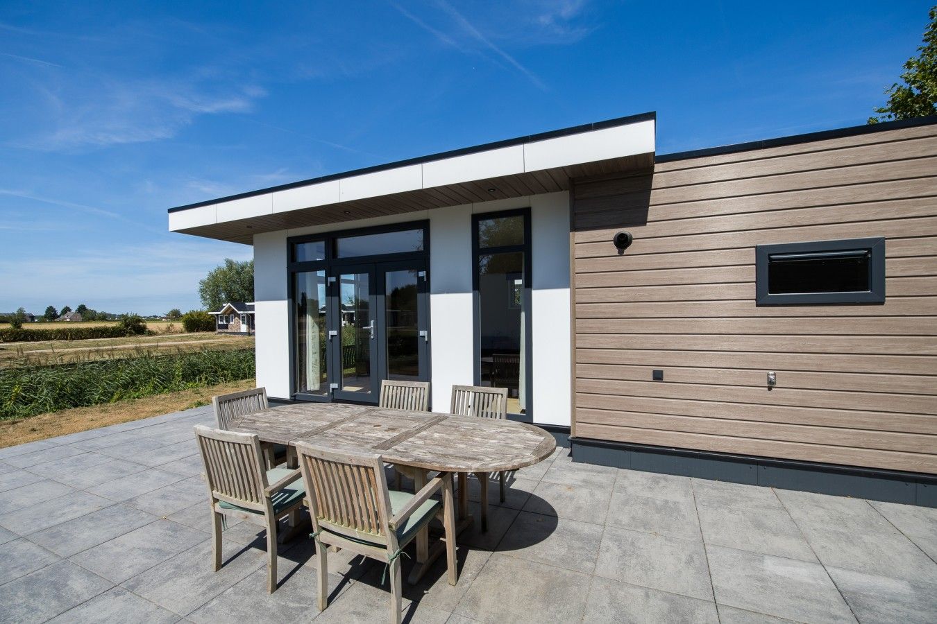 Una casa moderna con un patio, una mesa de comedor con sillas y vistas al campo.