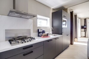 A modern kitchen with a gas stove, a coffee maker, and a sink. - Cube XL 71 | 4 persoons chalet in Zennewijnen (Zennewijnen)