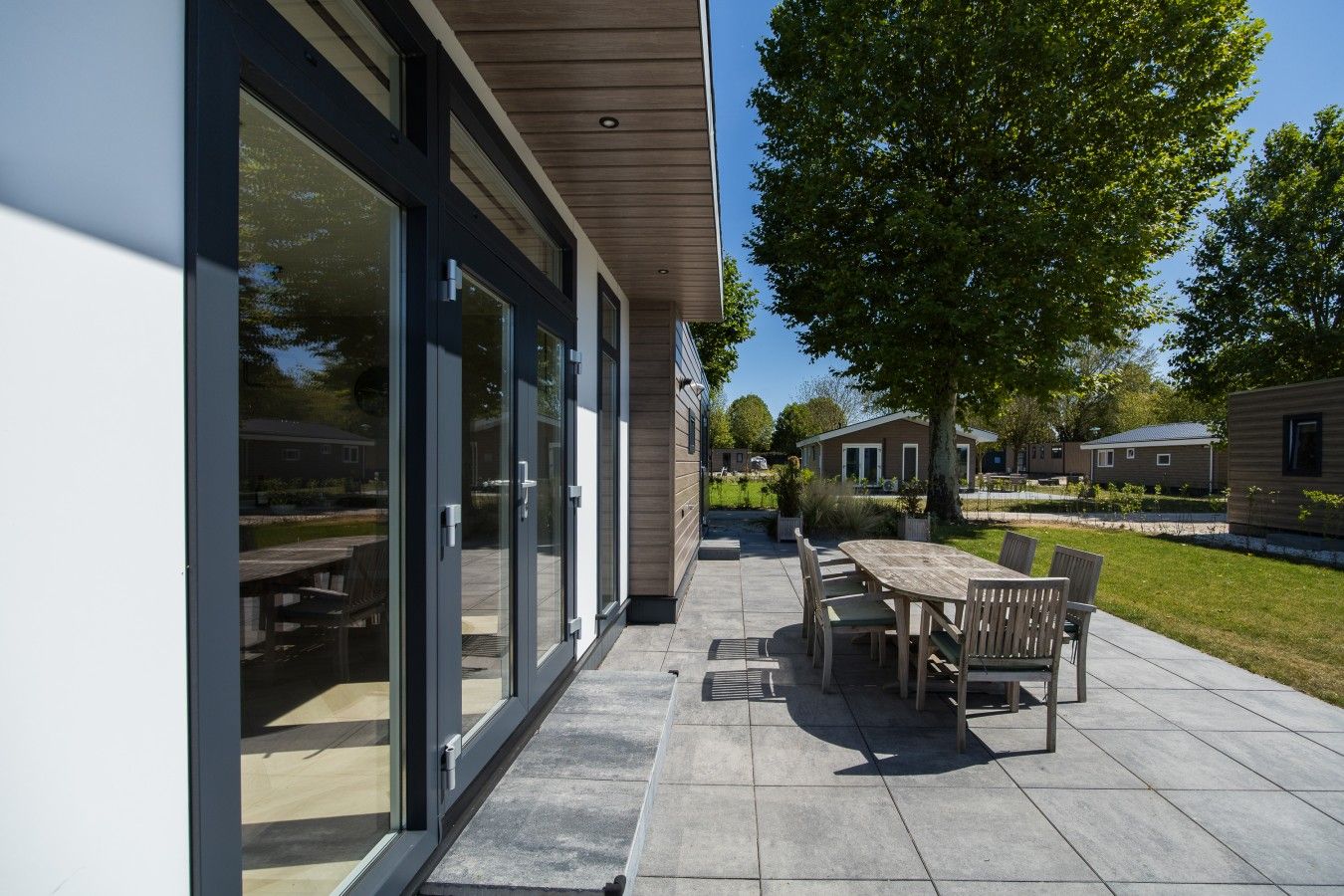 Ein moderner Außenbereich mit Terrassenmöbeln, ein großer Glastür-Eingang und ein gepflegter Rasen.