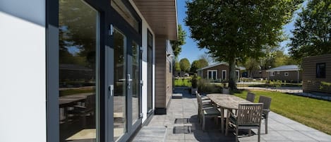 A modern outdoor patio area with a dining table and chairs, a large glass door entrance, and a well-maintained lawn.