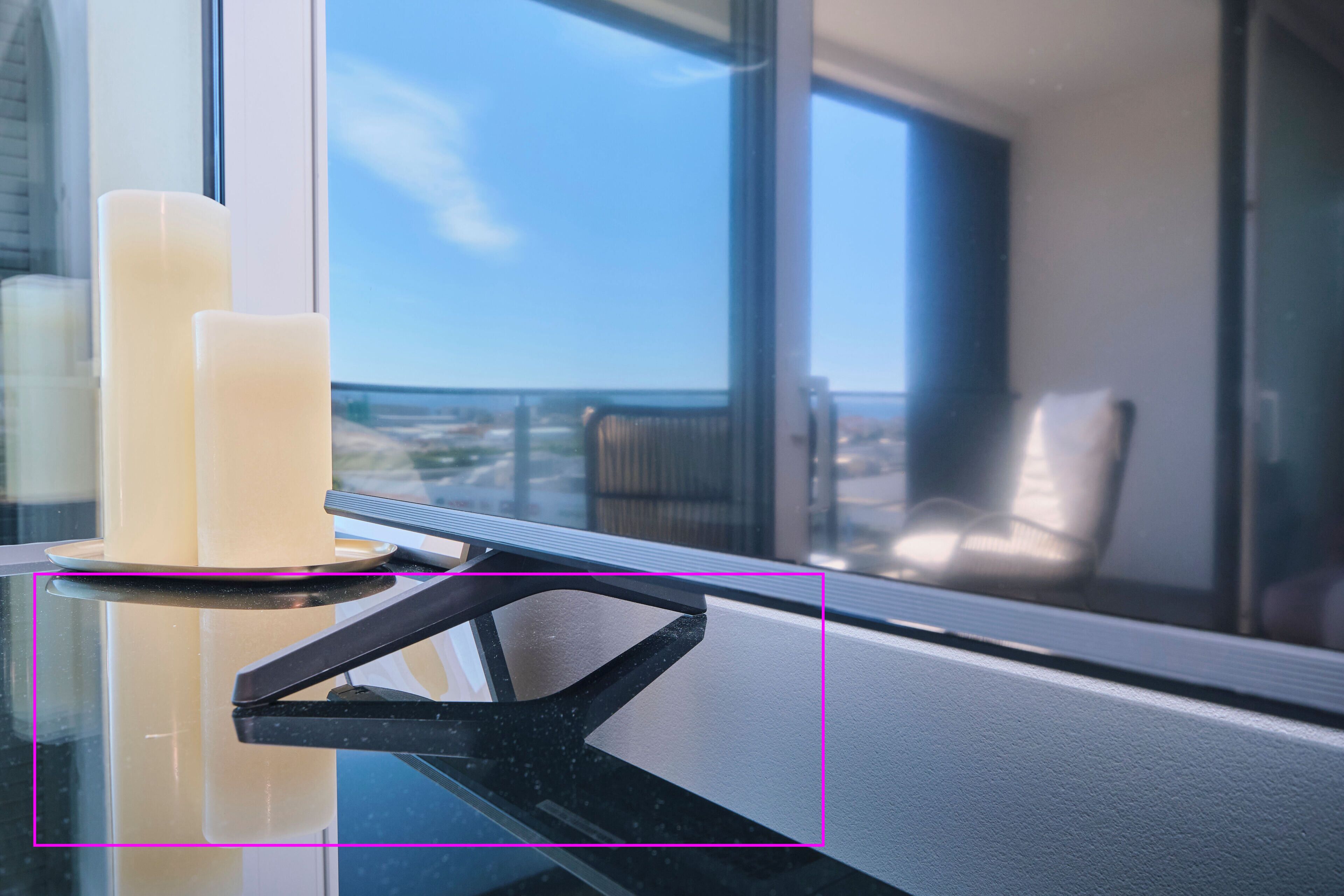 A window with a view of a balcony and chairs, a glass table with candles, and a window blind.