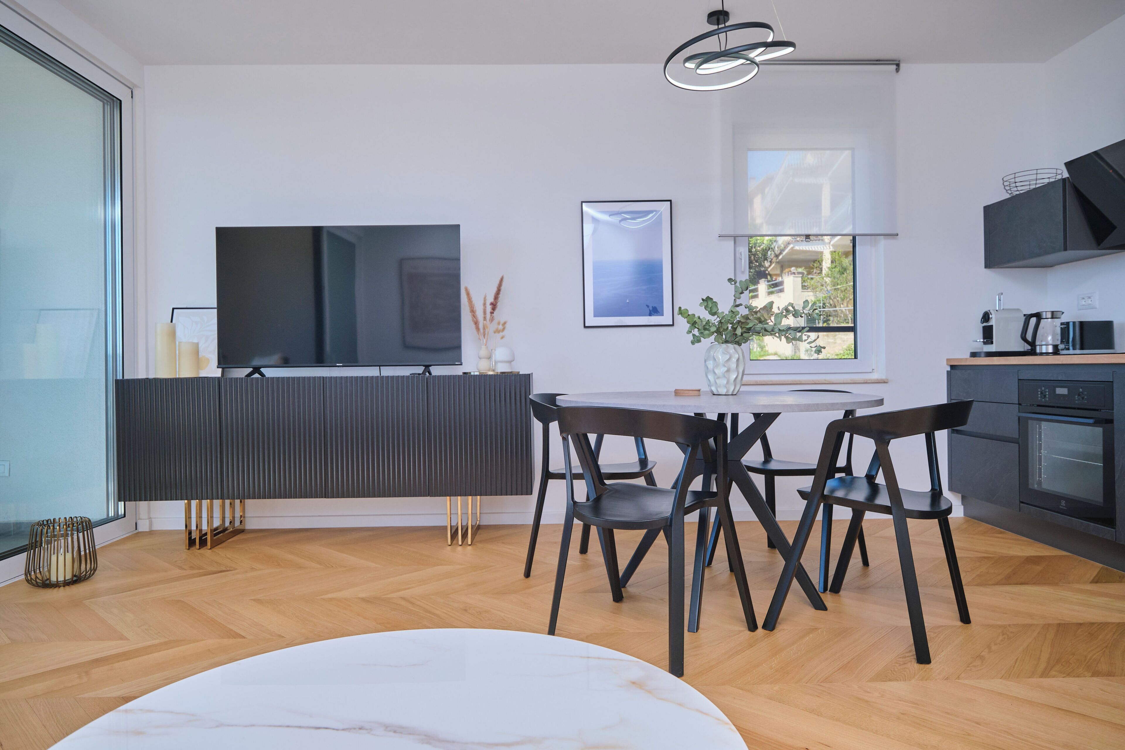 A modern kitchen with a TV, dining table, and chairs.