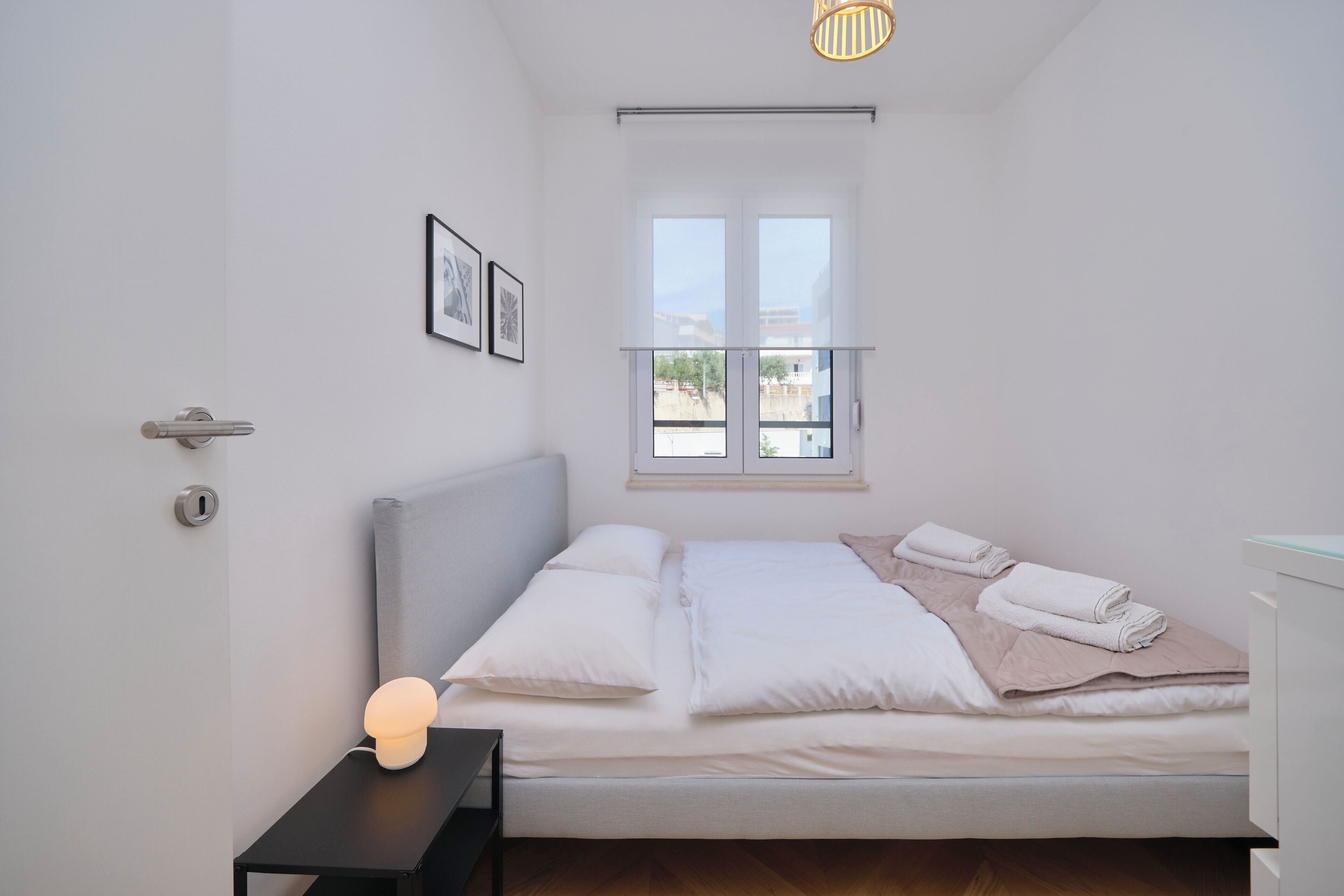 A bedroom with a bed, a bedside table with a lamp, a window with a view, and a door with a lock.