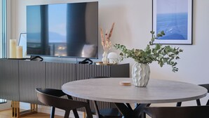 A modern dining area with a round table, chairs, a TV, a plant, and a framed picture on the wall. - City Lux Suite (Split)