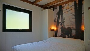 Une chambre à coucher avec un grand lit, une fenêtre, une lampe fixée au mur et un tableau représentant un cerf.