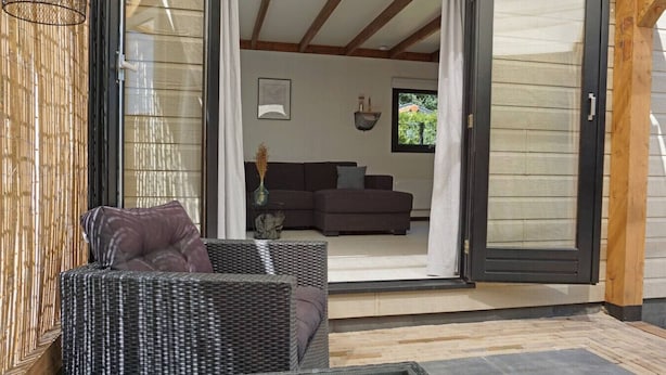 Une porte coulissante ouverte donne sur un espace de vie comprenant un canapé et un fauteuil en osier.