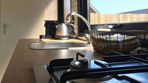 Une cuisine équipée d’une cuisinière à gaz, d’une bouilloire et d’une fenêtre donnant sur une terrasse en bois.