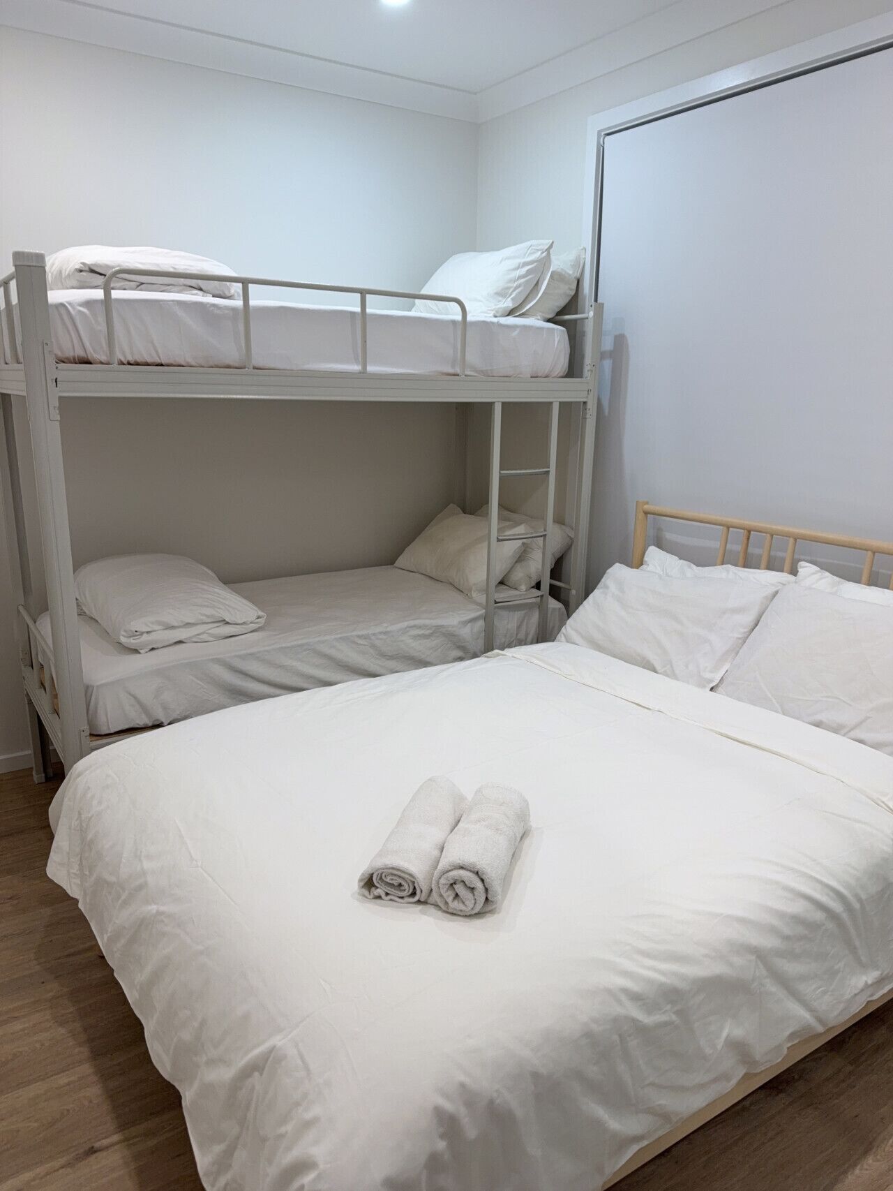 A bunk bed room with white bedding and two rolled towels on the lower bunk.