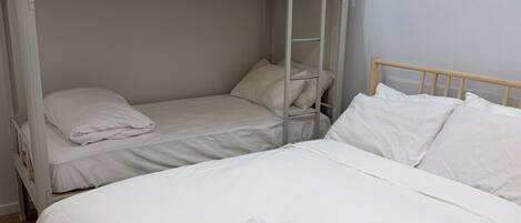 A bunk bed room with white bedding and two rolled towels on the lower bunk.
