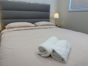 A neatly made bed with a grey headboard, two pillows, and a folded white towel on the bed. - Grand Family Estate for 20 people in Macarthur (Menangle Park)