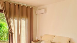 Un dormitorio con cama, cortinas, aire acondicionado, mesita de noche y lámpara.