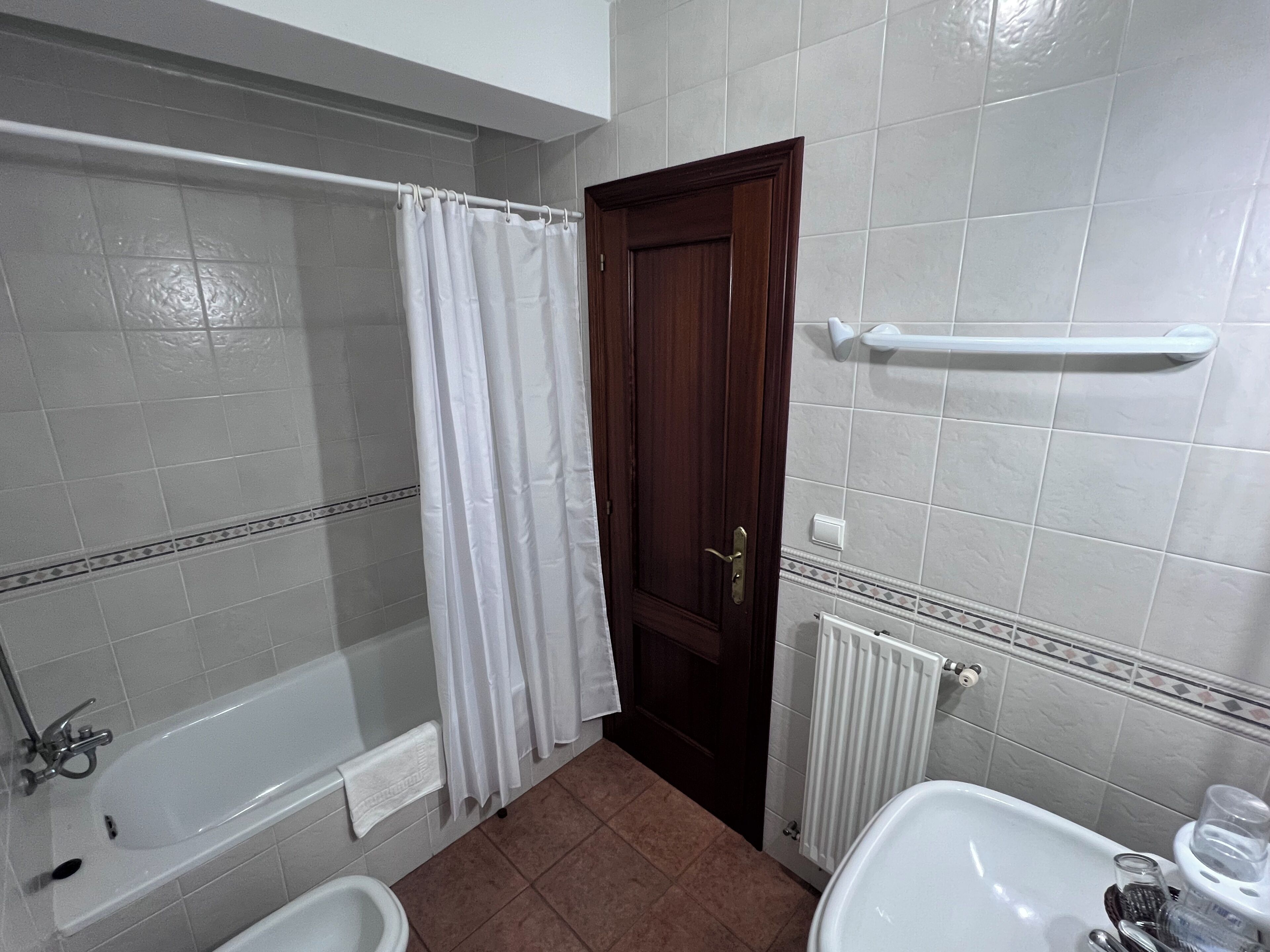 Een badkamer met een bad, douchegordijn, toilet, wastafel en radiator.