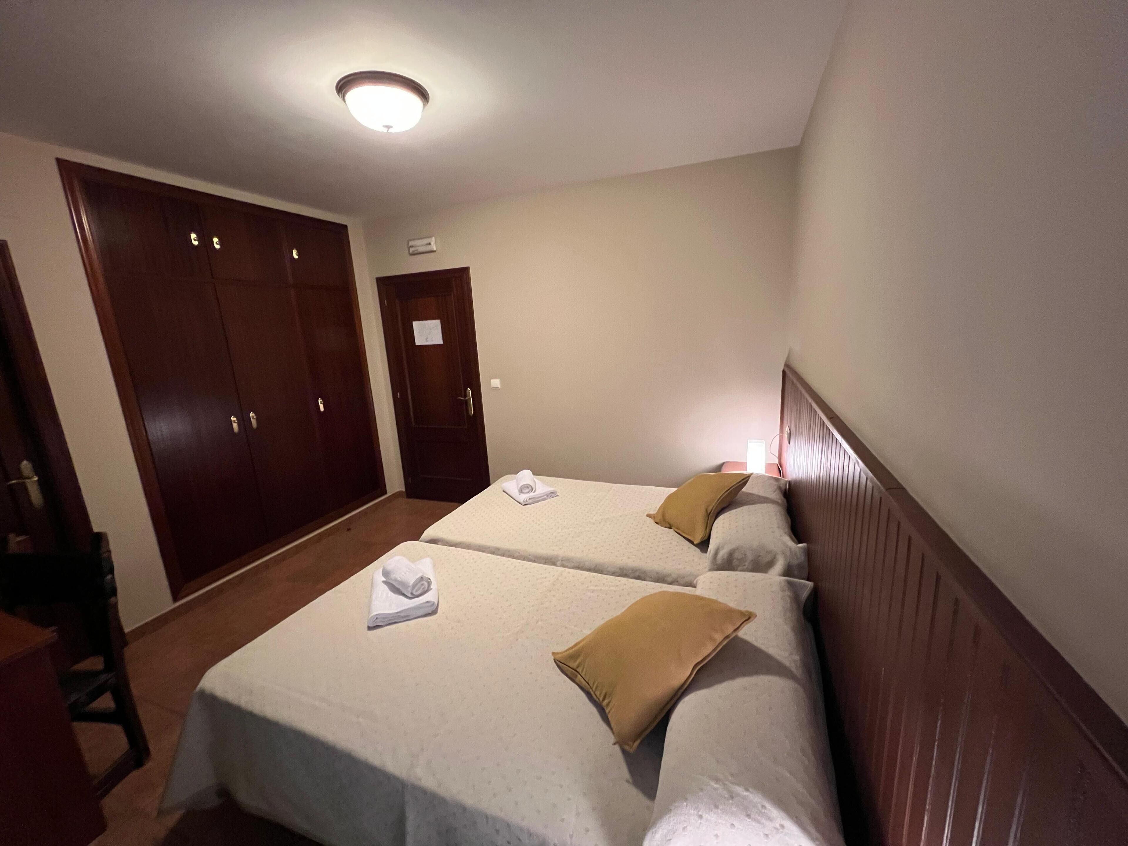 A hotel room with two beds, a wardrobe, and a desk.