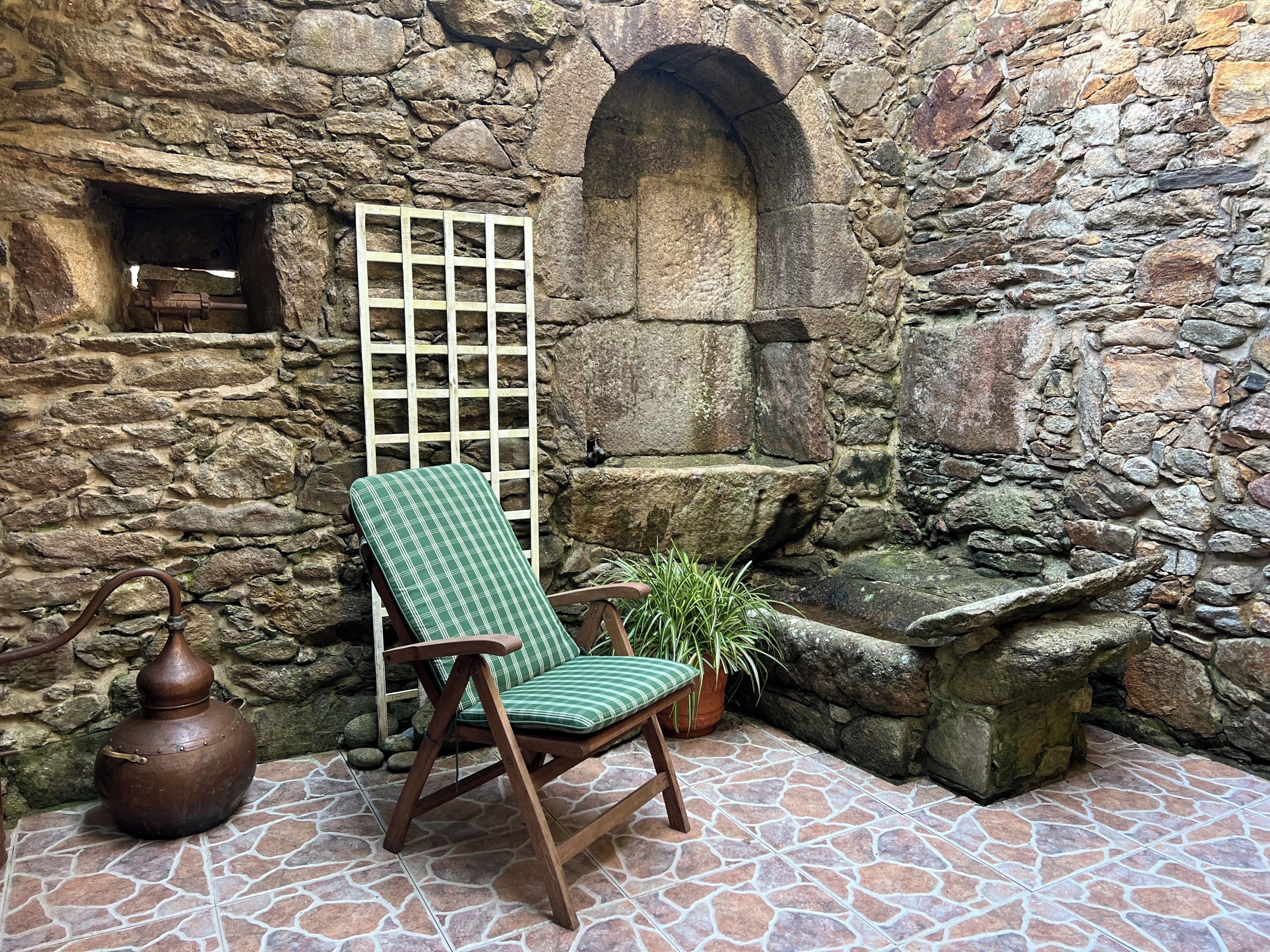 Habitació de parets de pedra amb una cadira de fusta, una planta en test i una llau de pedra.