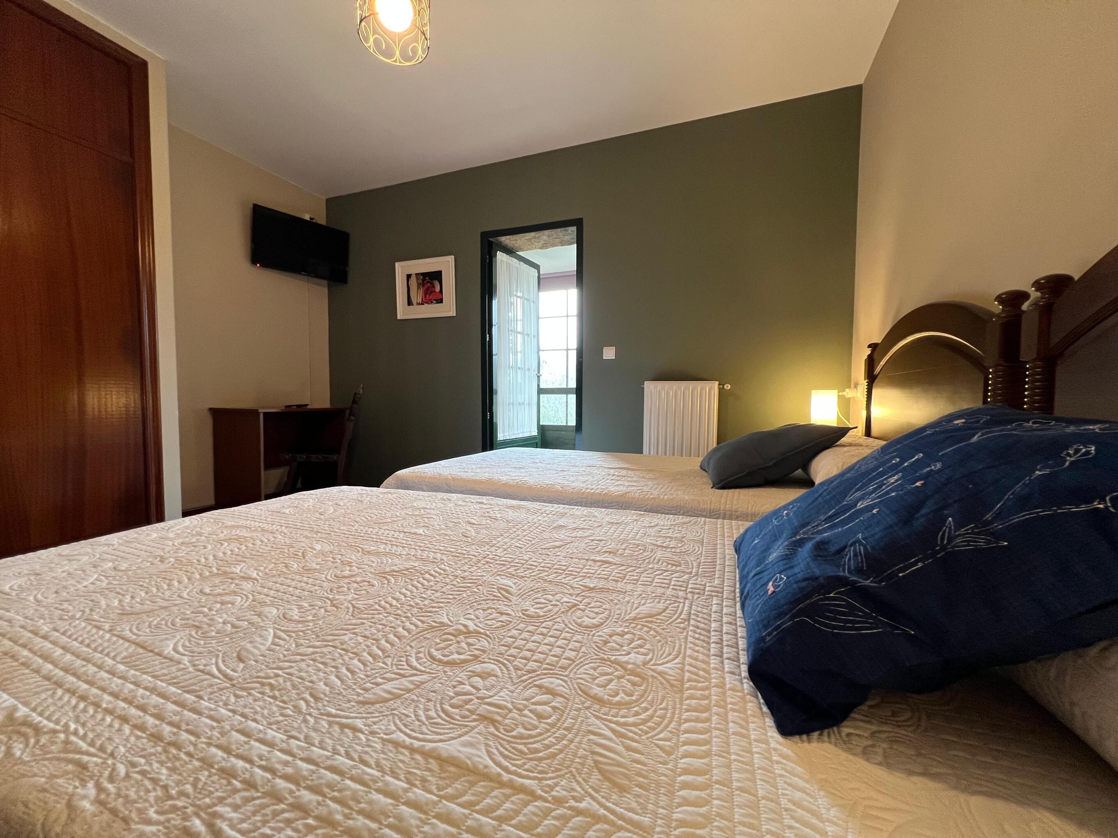 Un dormitorio con dos camas, un escritorio, una silla, un televisor y una puerta que da a un balcón.