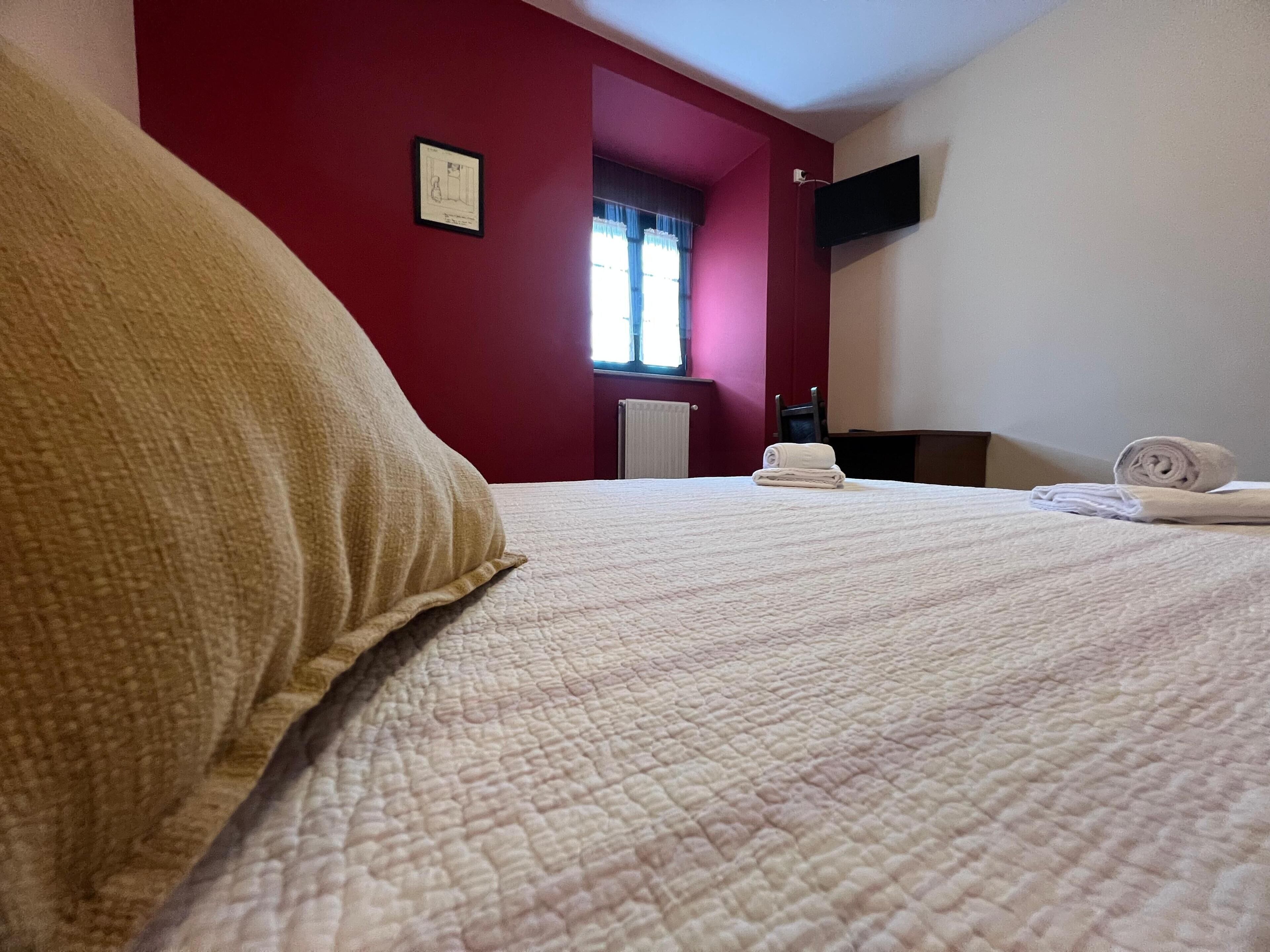 Una habitación de hotel con cama, ventana con cortinas, televisor de pantalla plana en la pared y radiador.