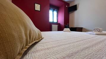 Una habitación de hotel con cama, ventana con cortinas, televisor de pantalla plana en la pared y radiador.