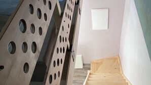 A wooden staircase with a metal handrail, a white wall with a small window, and a light-colored floor. - Fully-equipped self-contained apartment with Jacuzzi access (Marles-en-Brie)