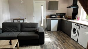 A compact living space with a sofa, a small table, a washing machine, and a kitchenette. - Fully-equipped self-contained apartment with Jacuzzi access (Marles-en-Brie)