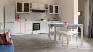 A modern kitchen with white cabinetry, a dining table with chairs, and a built-in oven. - Dependance Cugnana, surrounded by greenery and away from the chaos (Olbia)