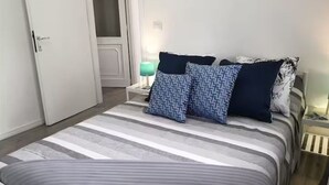 A bed with striped bedding, a bedside table with a lamp, and a door. - Dependance Cugnana, surrounded by greenery and away from the chaos (Olbia)