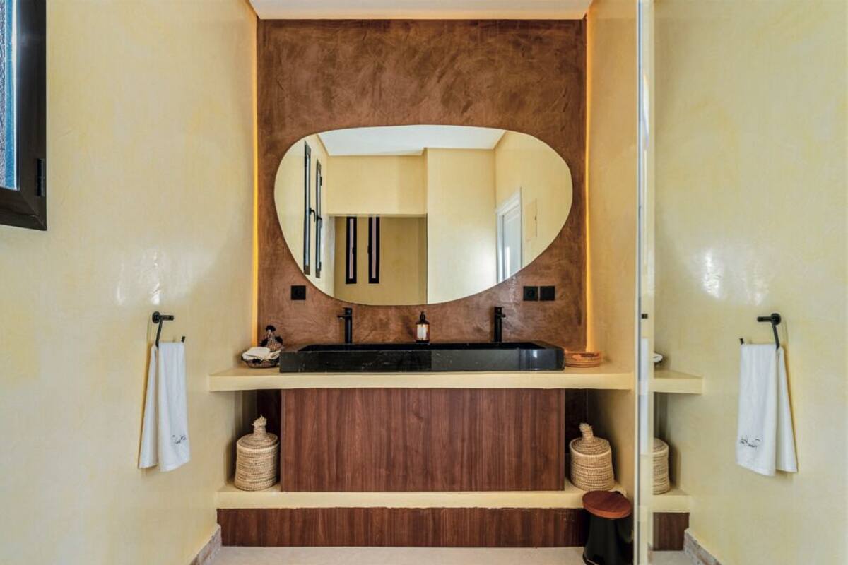 A bathroom with a large oval mirror, a black sink, wooden cabinets, and two towel racks.
