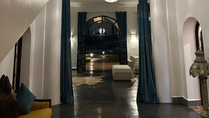 Ein geräumiger Innenraum mit Treppe, einer runden Deckenleuchte und Blick in einen dunklen Raum durch einen Bogen.