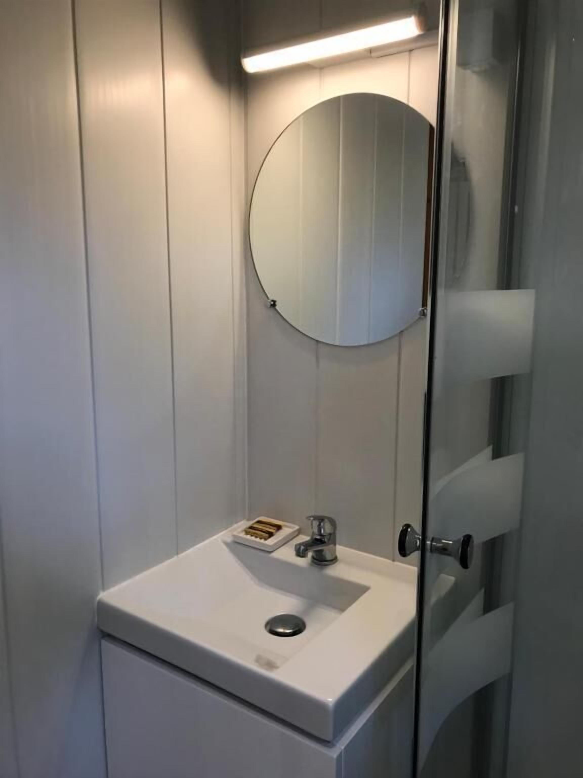 A bathroom with a white sink, a round mirror, and a glass shower enclosure.