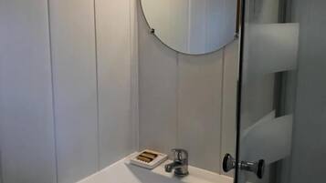 A bathroom with a white sink, a round mirror, and a glass shower enclosure.