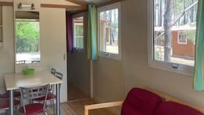 A room with a wooden ceiling, a red sofa, a dining table with chairs, and windows with curtains.