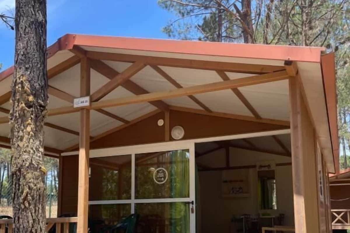 Une cabane en bois dotée d’un porche couvert, d’une porte d’entrée en verre et d’un petit espace extérieur aménagé pour s’asseoir.