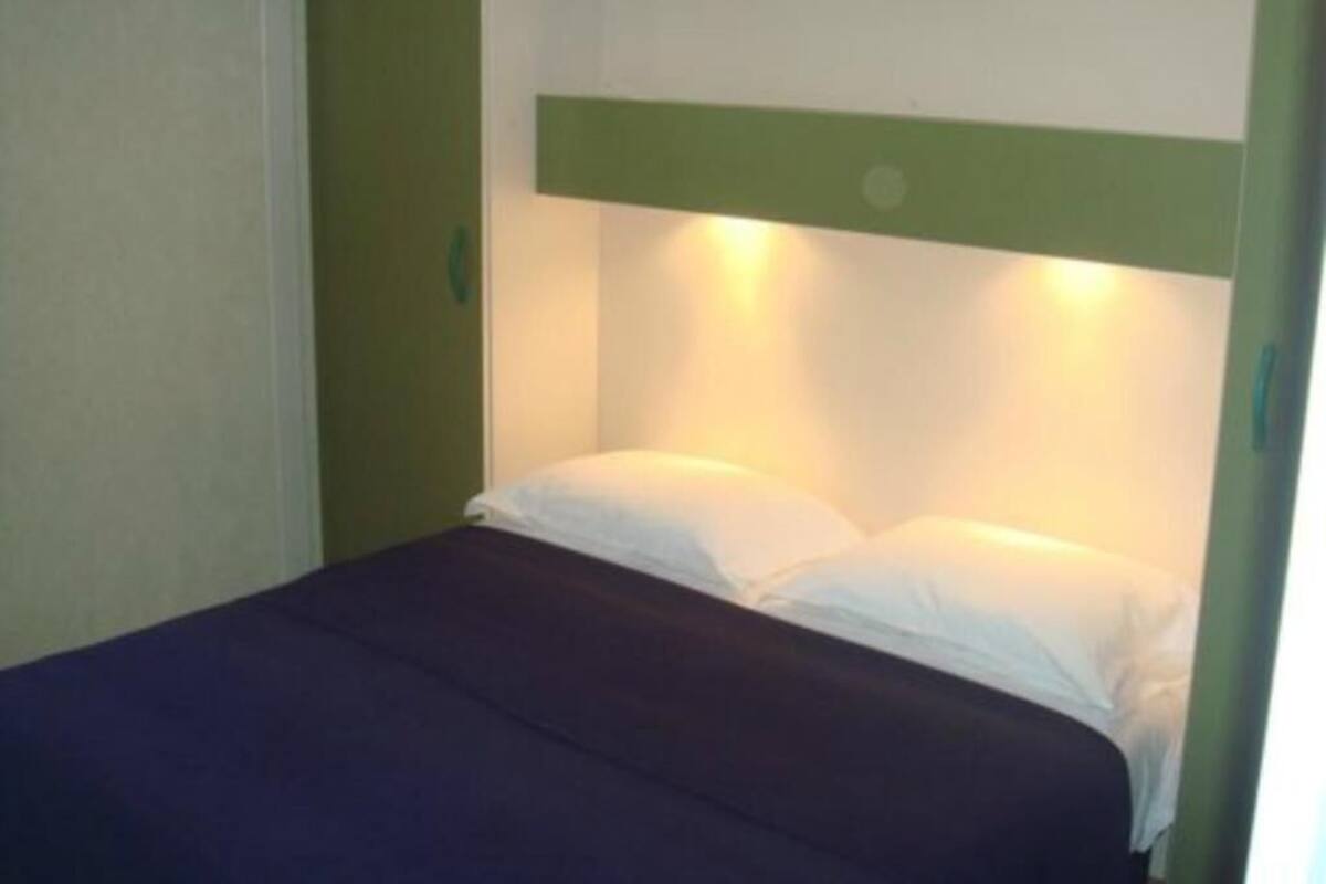 Un lit simple avec une tête de lit verte et du linge de lit blanc.