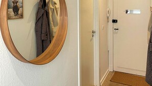 Un couloir avec un miroir encadré en bois, un porte-manteau sur lequel est accroché un manteau à carreaux, une porte blanche avec une poignée et un plancher en bois.