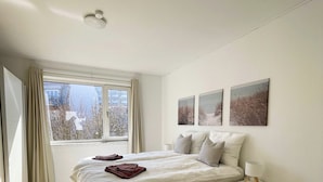 Une chambre à coucher avec un grand lit, une table de chevet, une commode, une fenêtre avec des rideaux et trois tableaux accrochés au mur.