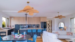 Eine moderne Küche mit Kochinsel, einem Essbereich mit rundem Tisch und einem Wohnbereich mit Sofa und Fernseher.