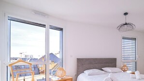 Ein Schlafzimmer mit einem Bett, einer Hängelampe, einem Fenster mit Jalousien und Blick auf Gebäude.