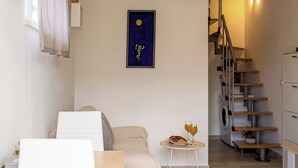 A modern living room with a sofa, a dining table, a staircase, and a wall-mounted artwork. -  1 bedroom apt in Korčula -Cozy Island Retreat /Walk Everywhere+Private Parking/ (Korčula)