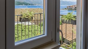 A view through a window with a metal railing, a clear sky, and a distant coastline. -  1 bedroom apt in Korčula -Cozy Island Retreat /Walk Everywhere+Private Parking/ (Korčula)