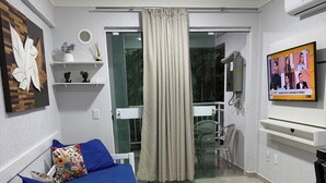 Et soveværelse med en hvid seng, et fjernsyn, en balkon med udsigt og en vægmonteret aircondition.