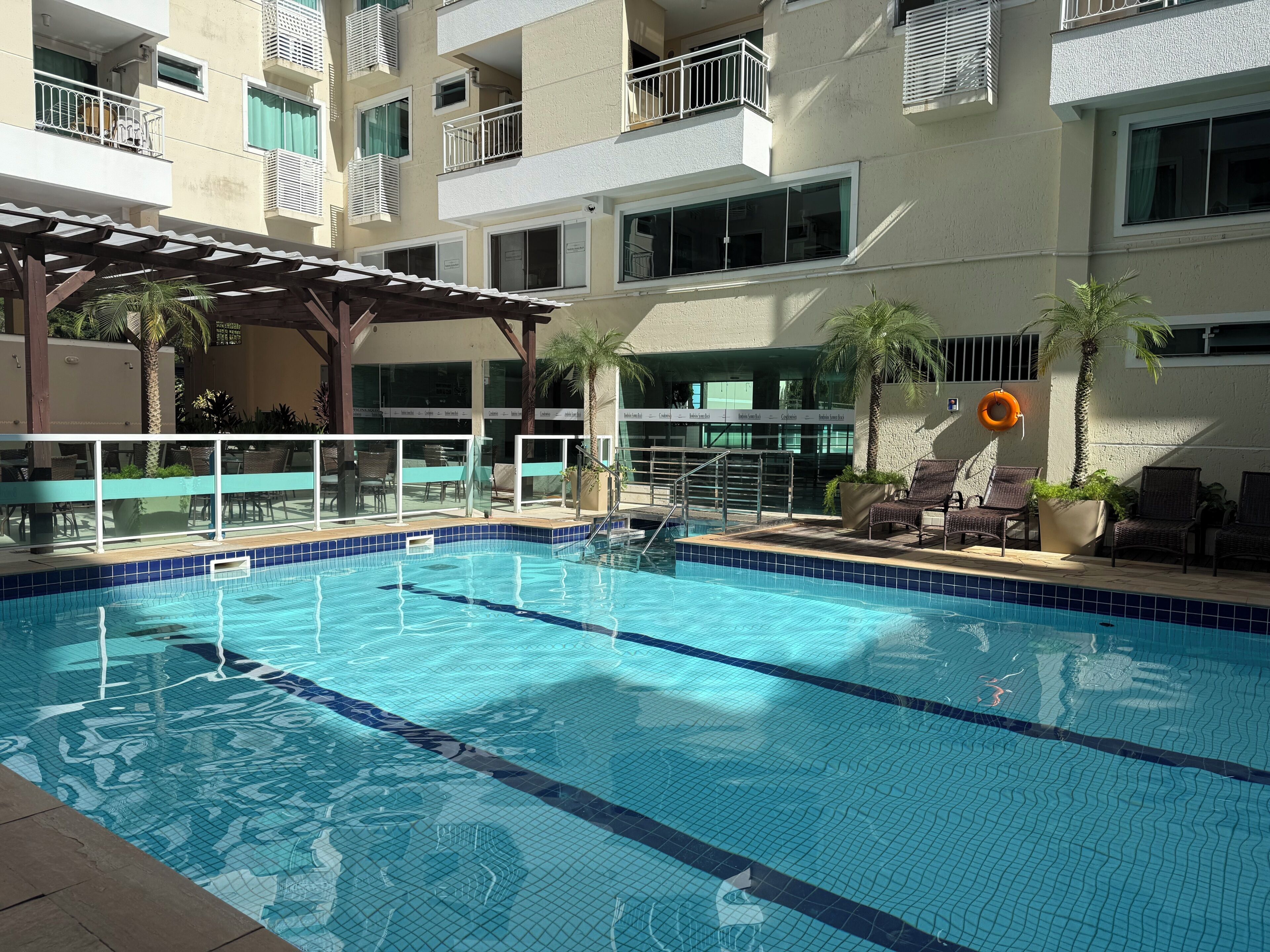 A swimming pool with clear blue water, surrounded by lounge chairs and a covered seating area.