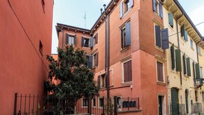 A row of traditional European buildings with balconies, a gate, and a tree in the foreground. - Filippini 10 (Verona)