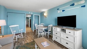 Una habitación con televisión, muebles blancos, una mecedora y dos tablas de remo en la pared.
