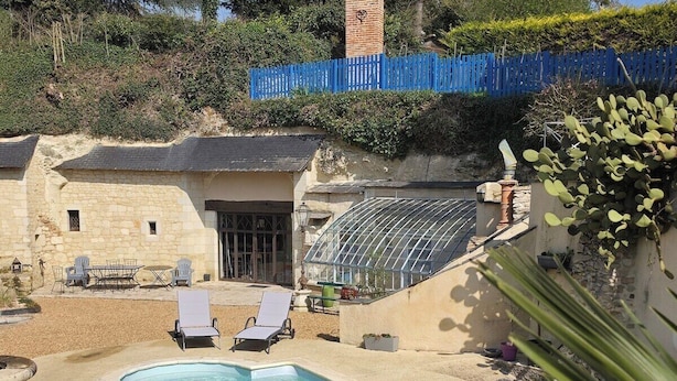A swimming pool with two lounge chairs, a greenhouse, and a blue fence.
