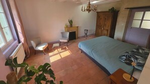 A bedroom with a bed, a chair, a small table, a fireplace, and a window.