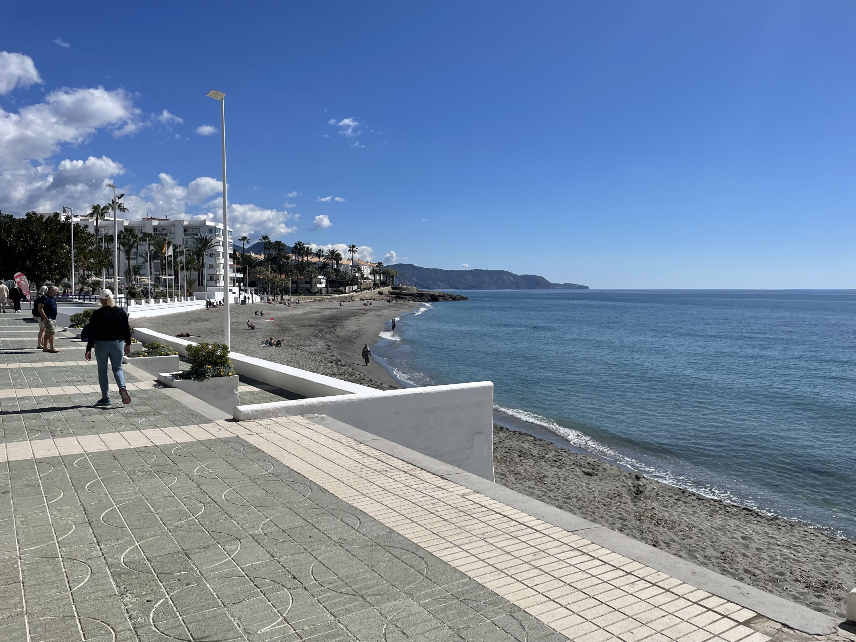 A coastal walkway with a paved path, beach, and ocean view.