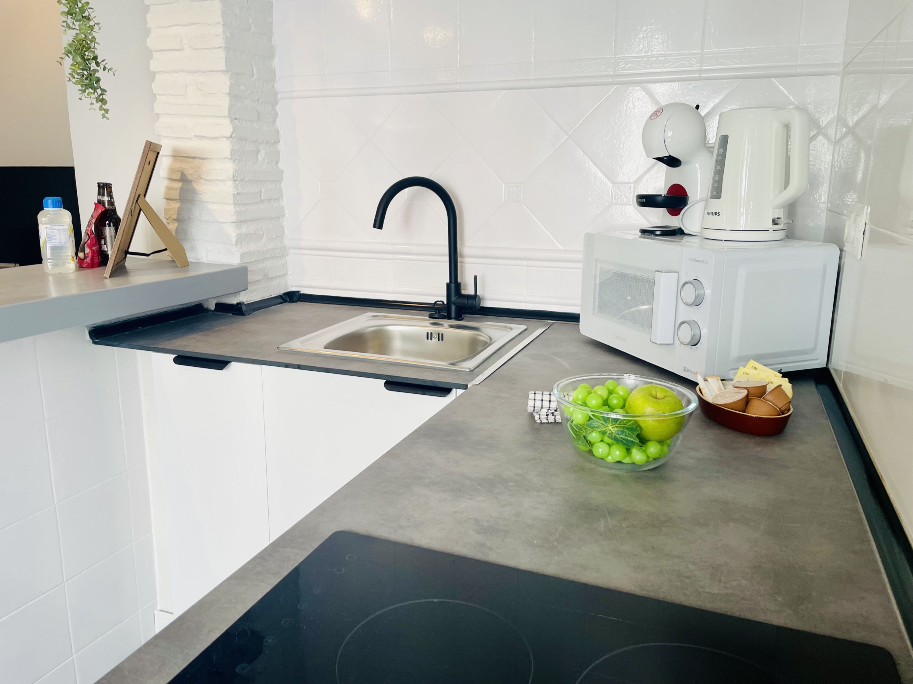 Una cocina moderna con un lavamanos integrado, un microondas y un tazón de manzanas verdes.